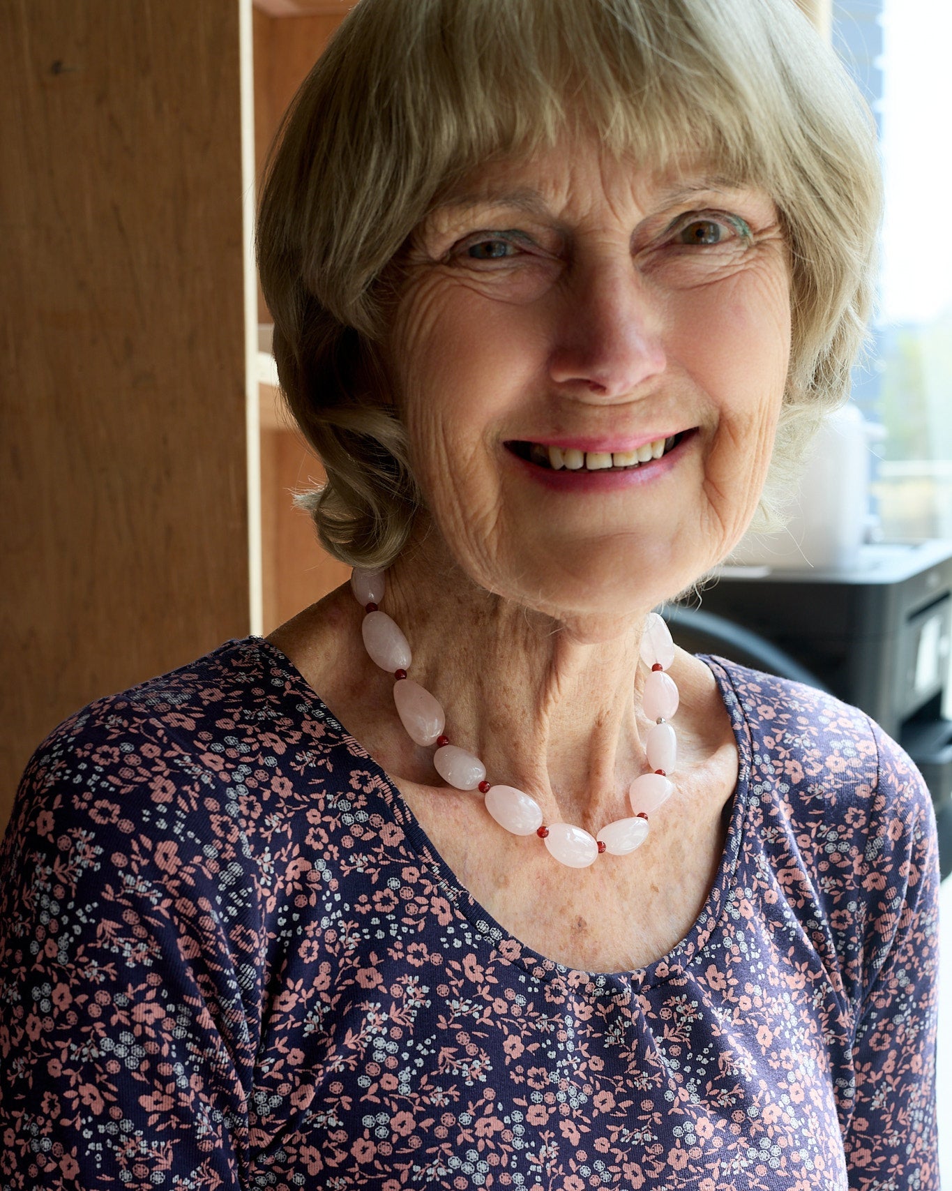 Woman wearing a floral blouse and pink rose quartz necklace indoors