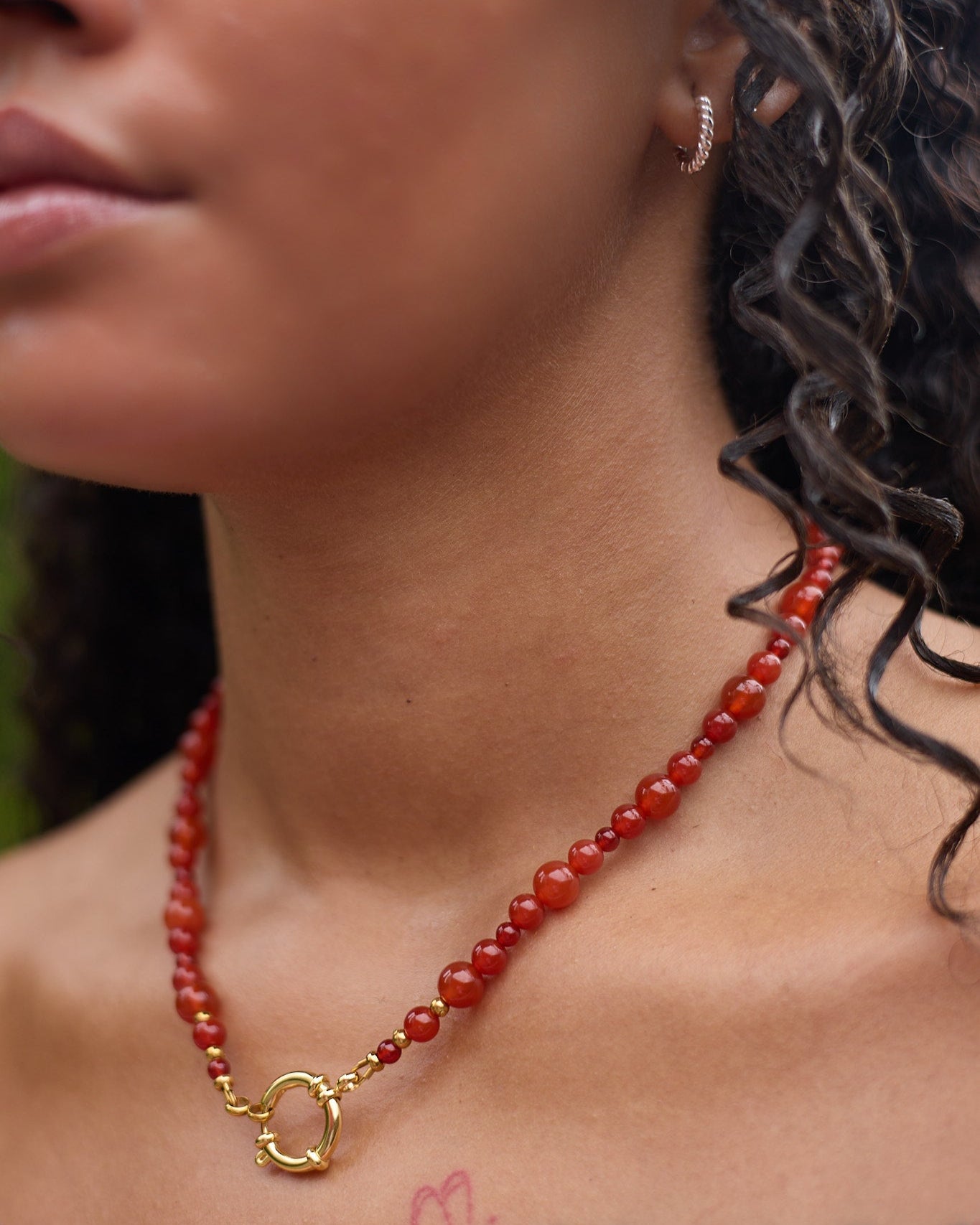 Close-up of a woman wearing a red beaded necklace with a gold clasp.