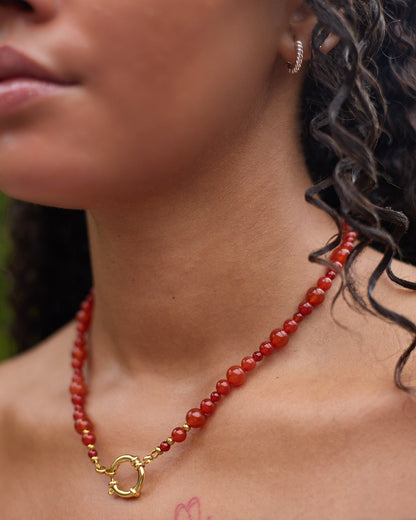 Close-up of a woman wearing a red beaded necklace with a gold clasp.